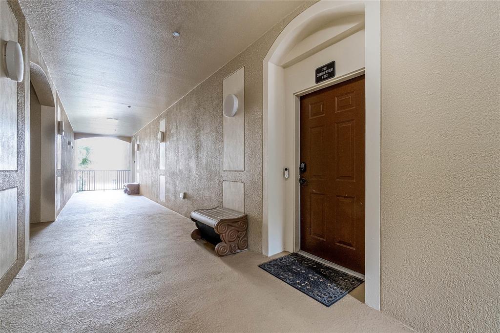 A brown door with a welcome mat sits in a beige outdoor apartment hallway — 7671 COMROW STREET UNIT 202, KISSIMMEE, FL