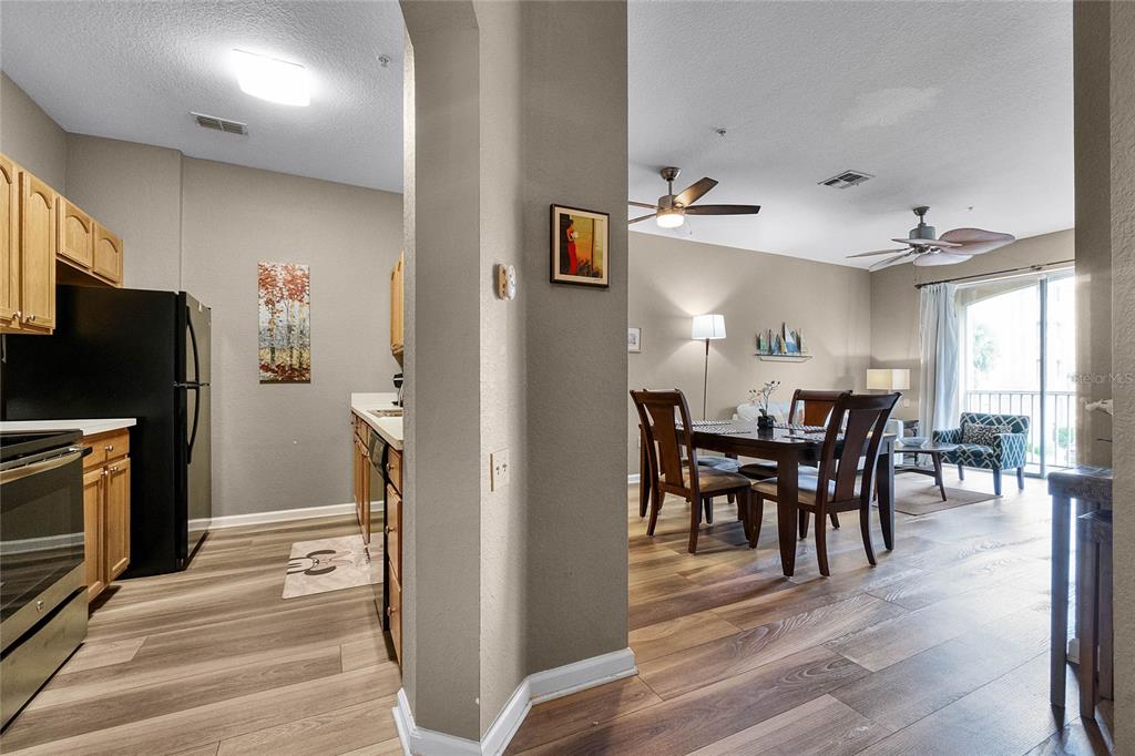 A kitchen with wood cabinets and black appliances opens into a dining and living area — 7671 COMROW STREET UNIT 202, KISSIMMEE, FL