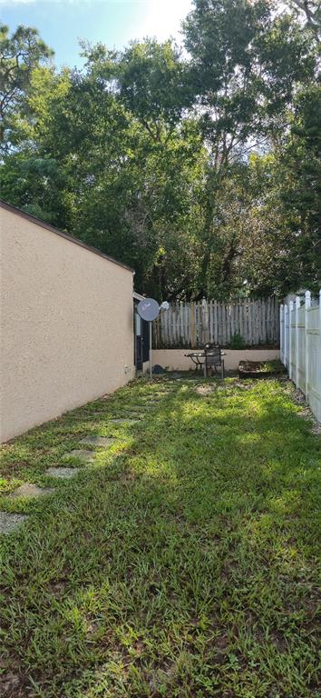 A side yard features a beige stucco wall, a stone path, and a wooden fence — 2214 OAK WIND DRIVE, HOLIDAY, FL