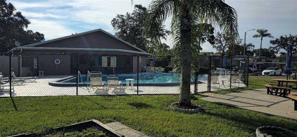A fenced outdoor swimming pool sits behind a building with a palm tree in front — 2214 OAK WIND DRIVE, HOLIDAY, FL