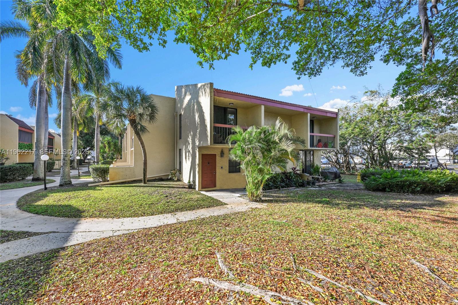 A two-story tan apartment building features a red front door and balconies under large trees — 781 SE 1st Way # 79, Deerfield Beach FL 33441, DEERFIELD BEACH, FL