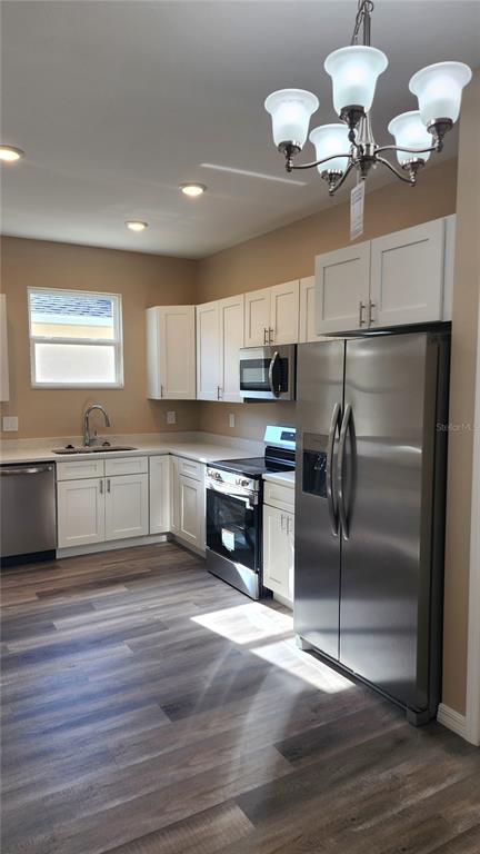 A kitchen with white cabinets, stainless steel appliances, and wood-look flooring under a chandelier — 2043 MULLET ROAD, AUBURNDALE, FL