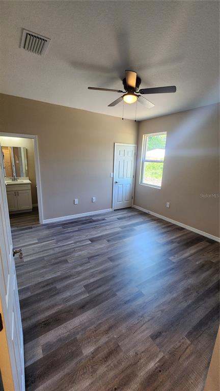 A bedroom with gray wood-look flooring, a ceiling fan, a window, and an attached bathroom — 2043 MULLET ROAD, AUBURNDALE, FL