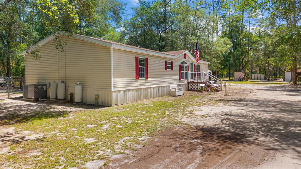 A tan manufactured home with red shutters sits on a sandy lot with tall trees — 106 ARROWHEAD POINT ROAD, HAWTHORNE, FL