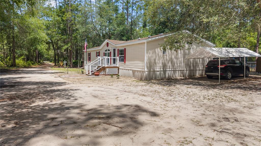 A single-story manufactured home with beige siding, red shutters, and a metal carport — 106 ARROWHEAD POINT ROAD, HAWTHORNE, FL
