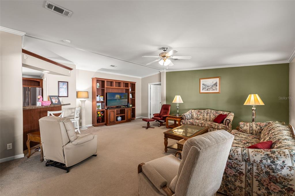 A living room features beige carpet, a large wooden entertainment center, and floral patterned sofas — 82085 1ST AVENUE N UNIT 85, PINELLAS PARK, FL