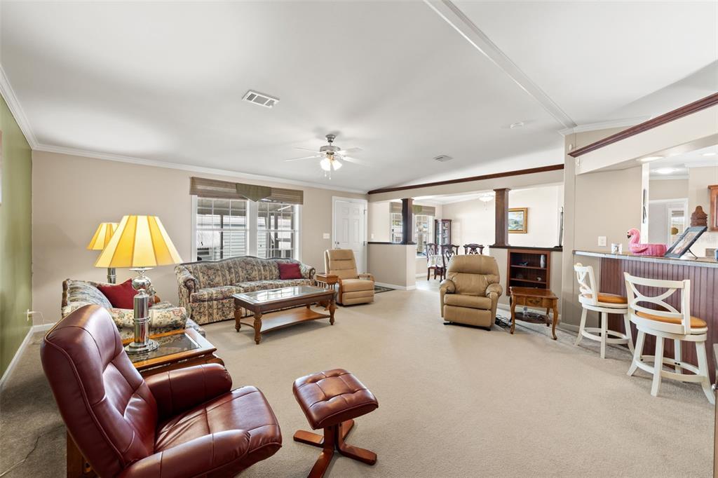 A living room with beige carpet, a floral sofa, leather recliners, and a breakfast bar — 82085 1ST AVENUE N UNIT 85, PINELLAS PARK, FL