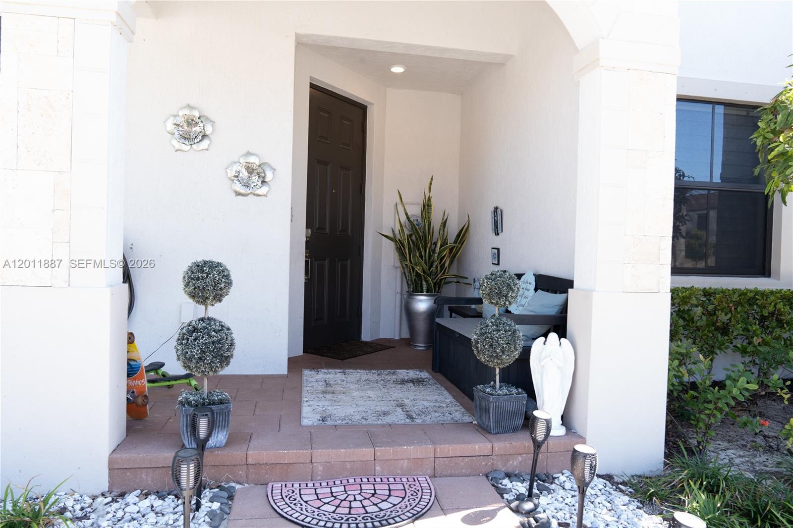 A front porch features a dark door, potted topiary plants, and a small bench — 10599 W 33rd Ct, Hialeah FL 33018, HIALEAH, FL