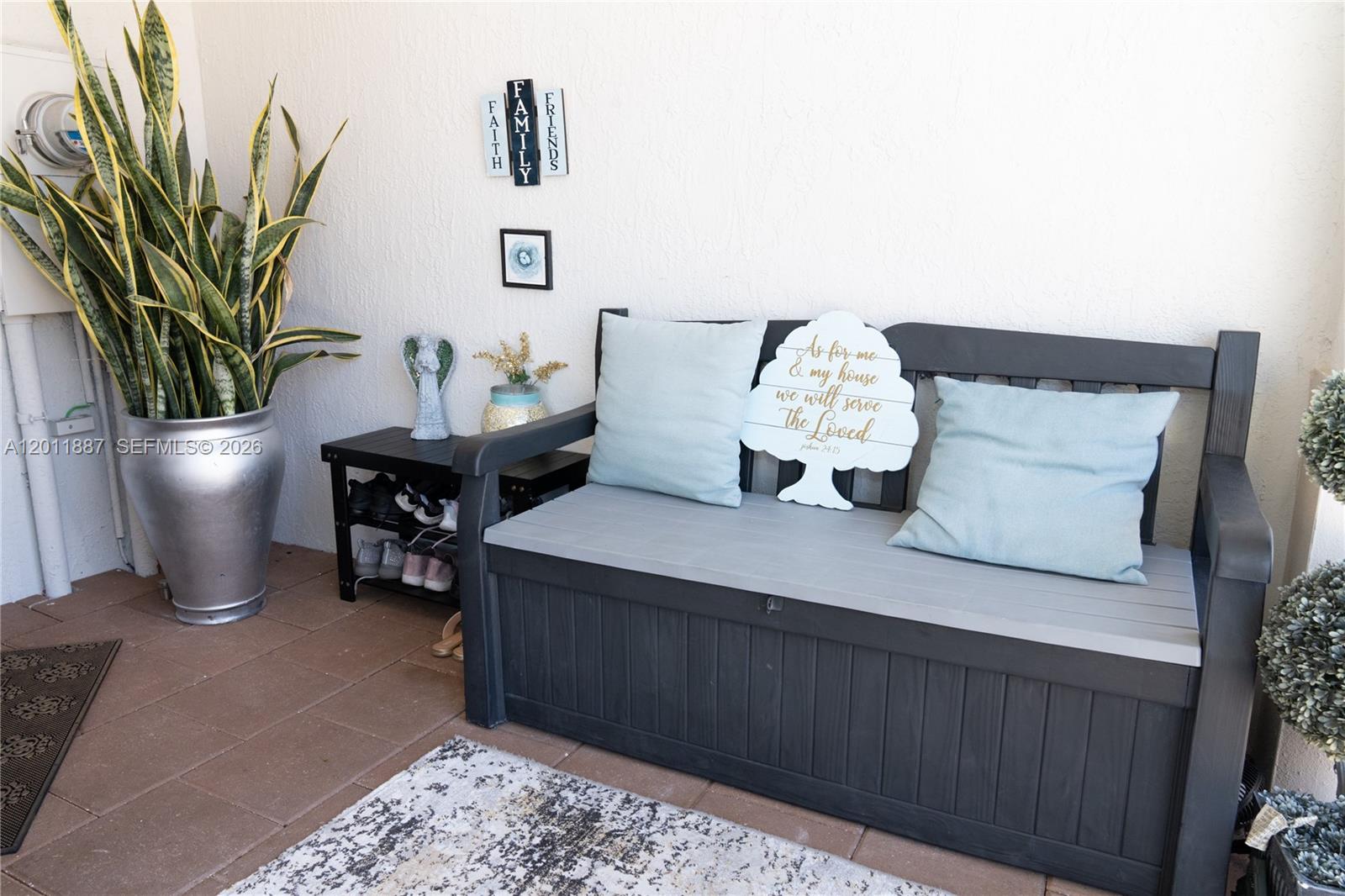 A covered patio features a dark storage bench with light blue pillows and a large plant — 10599 W 33rd Ct, Hialeah FL 33018, HIALEAH, FL