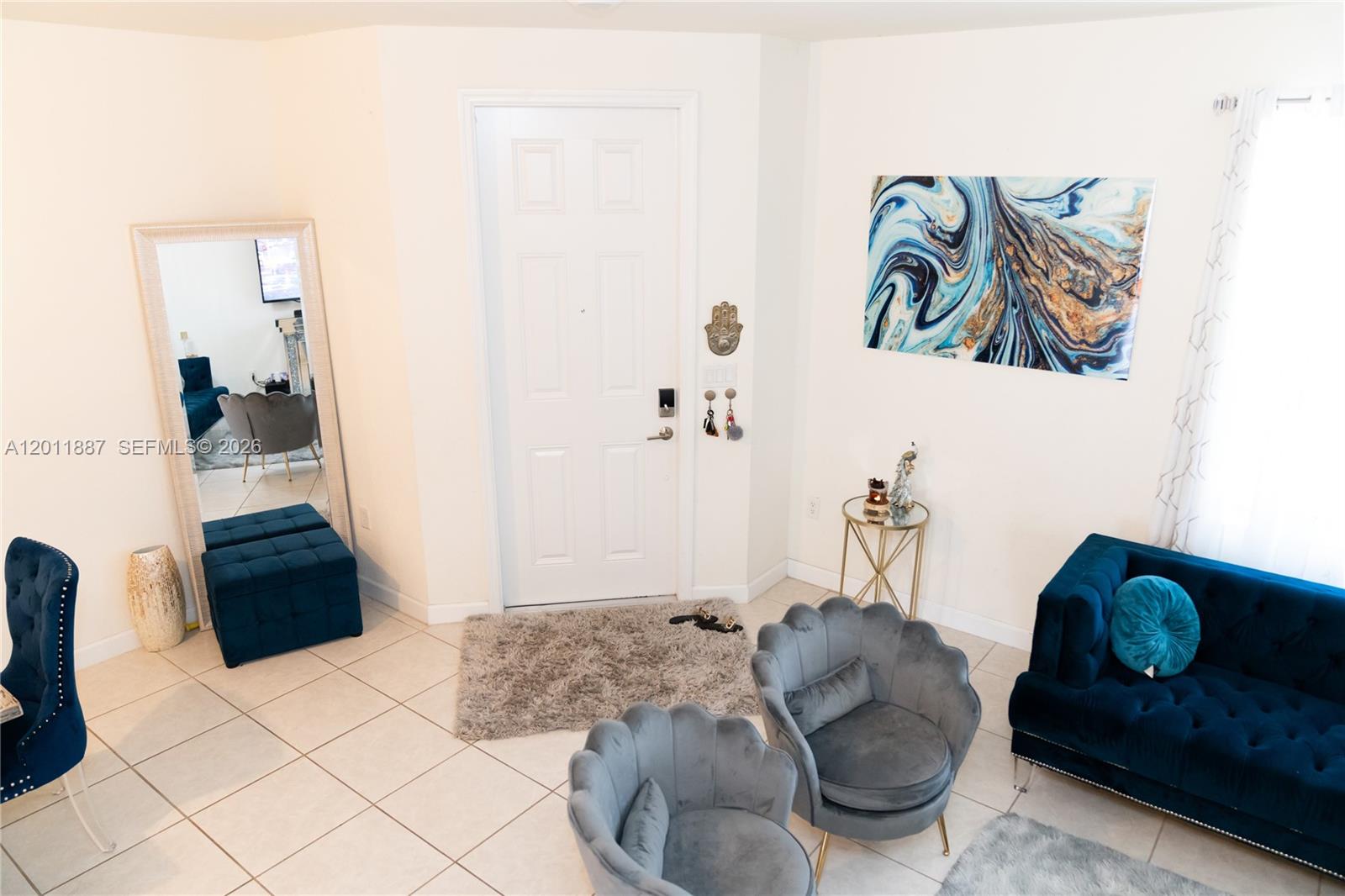 This living room features a white front door, blue velvet furniture, and a large mirror — 10599 W 33rd Ct, Hialeah FL 33018, HIALEAH, FL