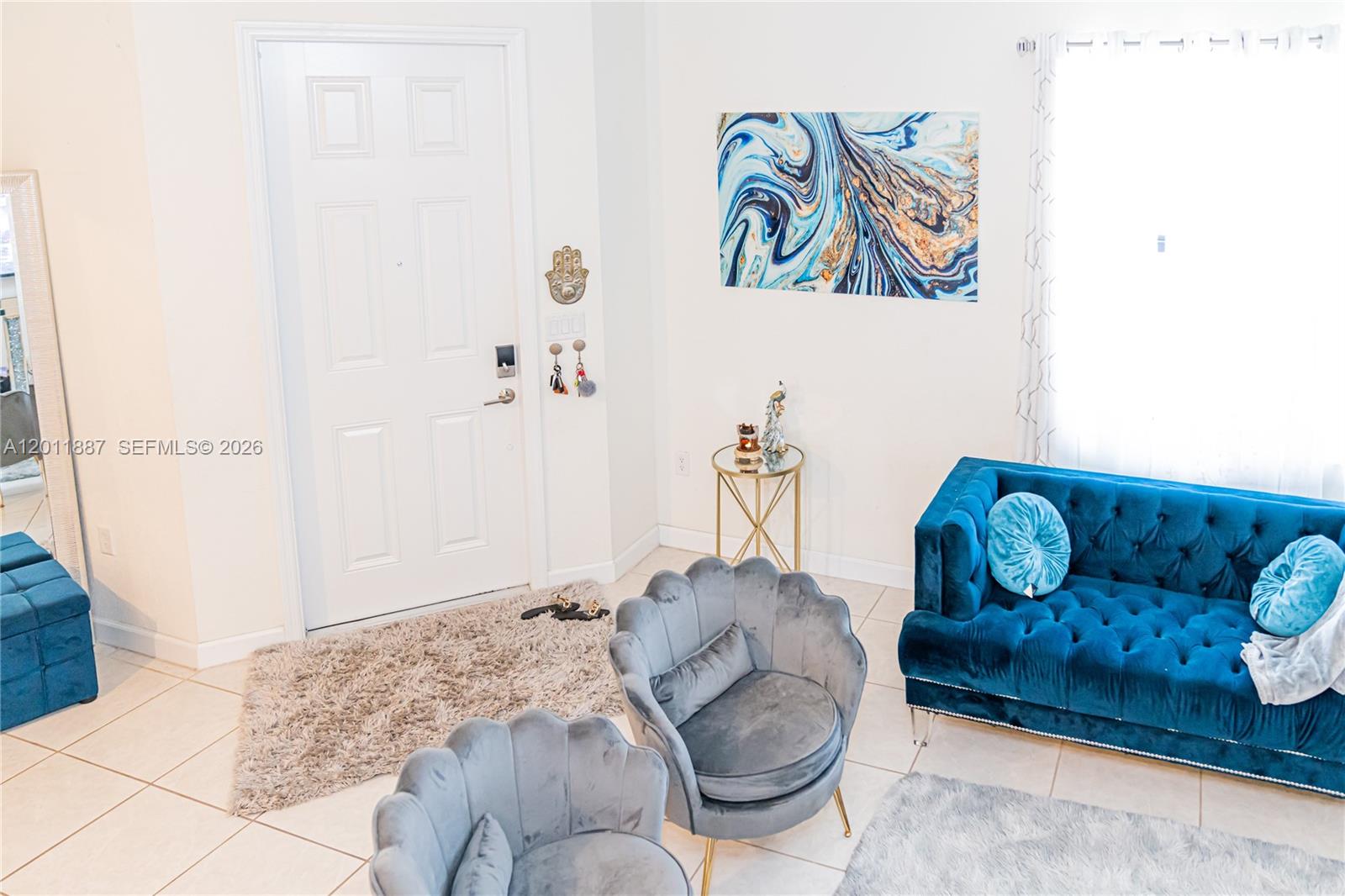 A living room features a blue tufted sofa, two grey chairs, and a white door — 10599 W 33rd Ct, Hialeah FL 33018, HIALEAH, FL