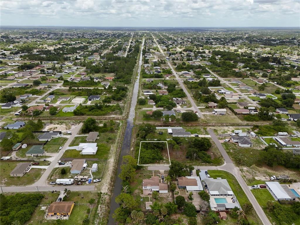 An aerial view shows a vacant, rectangular lot outlined in white within a residential neighborhood — 3105 BRIAN AVENUE S, LEHIGH ACRES, FL