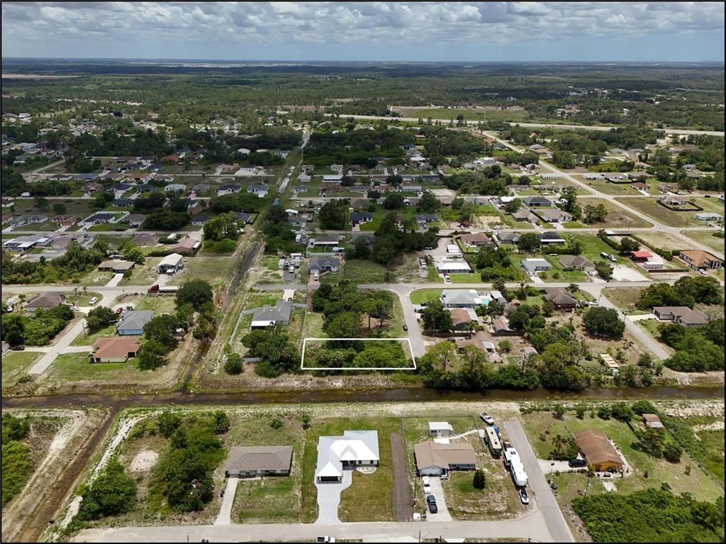 An aerial view shows a vacant, tree-covered residential lot outlined in white near a canal — 3105 BRIAN AVENUE S, LEHIGH ACRES, FL