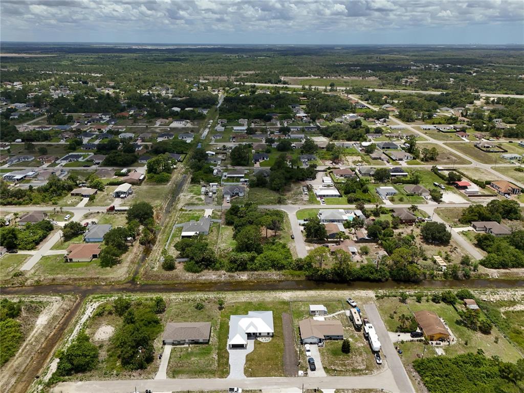 An aerial view shows a residential neighborhood with single-family homes, paved roads, and drainage canals — 3105 BRIAN AVENUE S, LEHIGH ACRES, FL