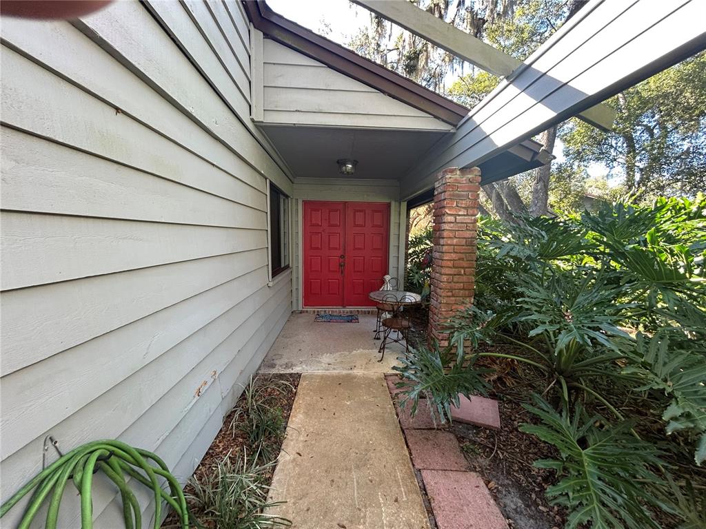 A concrete walkway leads to a covered entryway with red double doors and brick columns — 906 VILLAGE GREEN ROAD, DELAND, FL