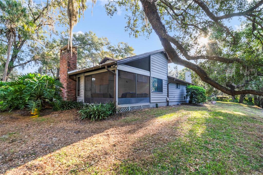 A gray house with a screened-in porch and a brick chimney sits under large trees — 906 VILLAGE GREEN ROAD, DELAND, FL