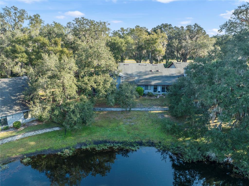 An aerial view shows a house with a gray roof situated behind a small pond — 906 VILLAGE GREEN ROAD, DELAND, FL