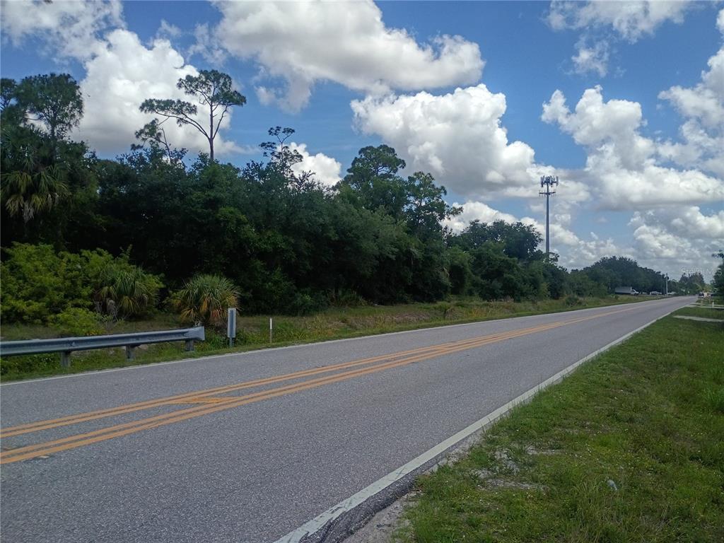 A paved road stretches past a wooded lot under a bright, cloudy sky — 6255 TAYLOR ROAD, PUNTA GORDA, FL
