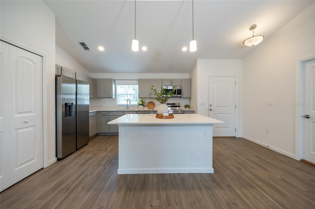 A kitchen features gray cabinets, stainless steel appliances, a white island, and wood-look flooring — 196 FRONTIER DRIVE, PALM COAST, FL