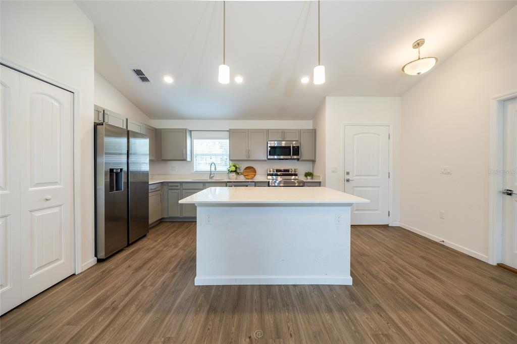 A kitchen features gray cabinets, stainless steel appliances, a white island, and wood-look flooring — 196 FRONTIER DRIVE, PALM COAST, FL