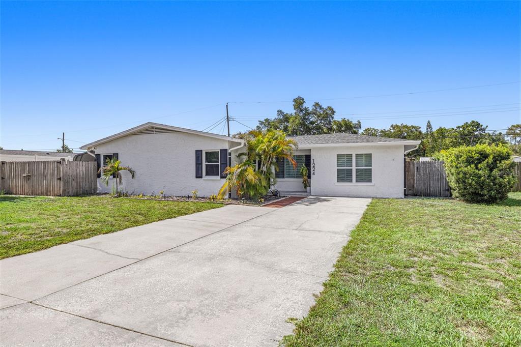 A single-story white house with a concrete driveway and a wooden fence — 1224 80TH AVENUE N, ST PETERSBURG, FL