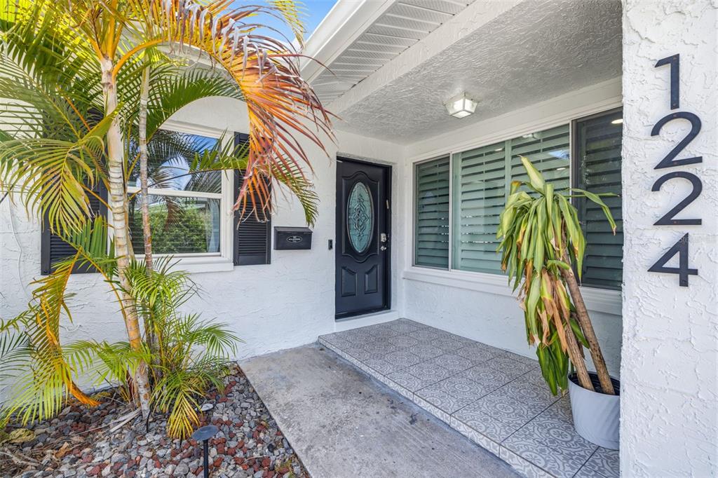 A front entryway features a black door, tiled porch, and potted plants under a palm tree — 1224 80TH AVENUE N, ST PETERSBURG, FL