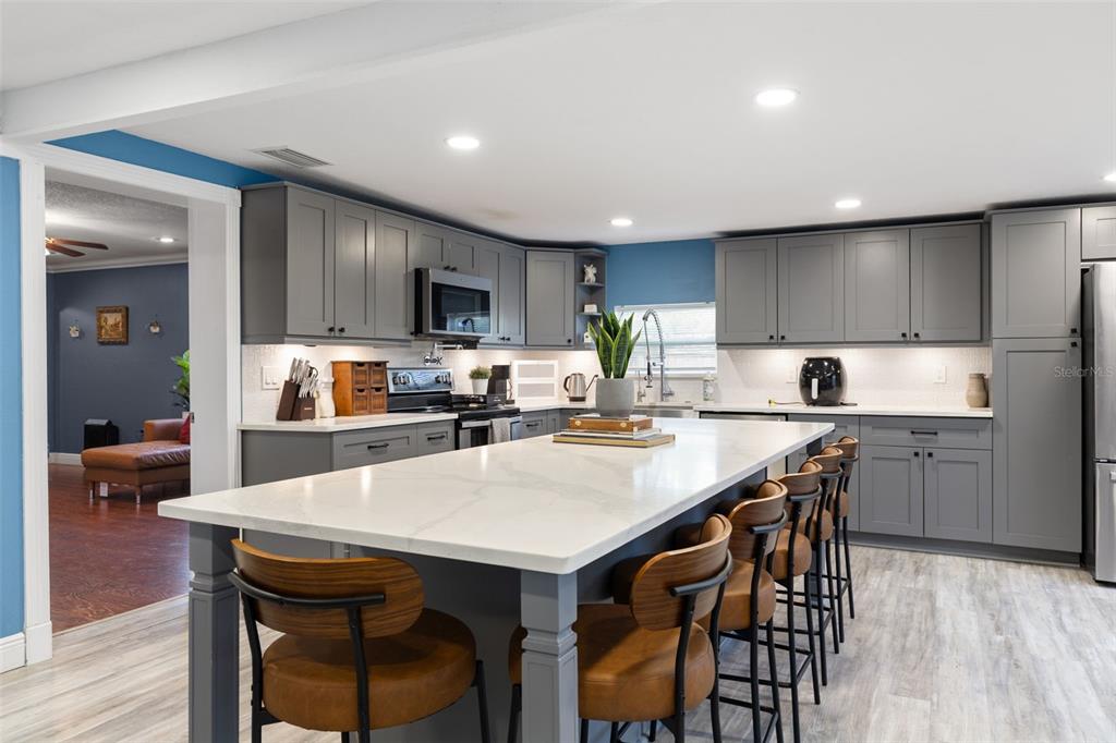 A modern kitchen features gray cabinets, a large white quartz island, and brown bar stools — 1224 80TH AVENUE N, ST PETERSBURG, FL