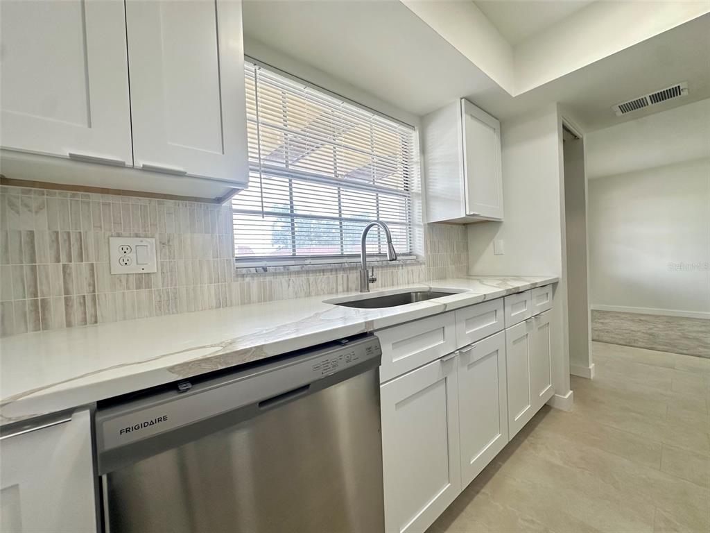 A kitchen features white cabinets, a stainless steel dishwasher, and a marble-patterned countertop — 1845 S HIGHLAND AVENUE UNIT 6-11, CLEARWATER, FL