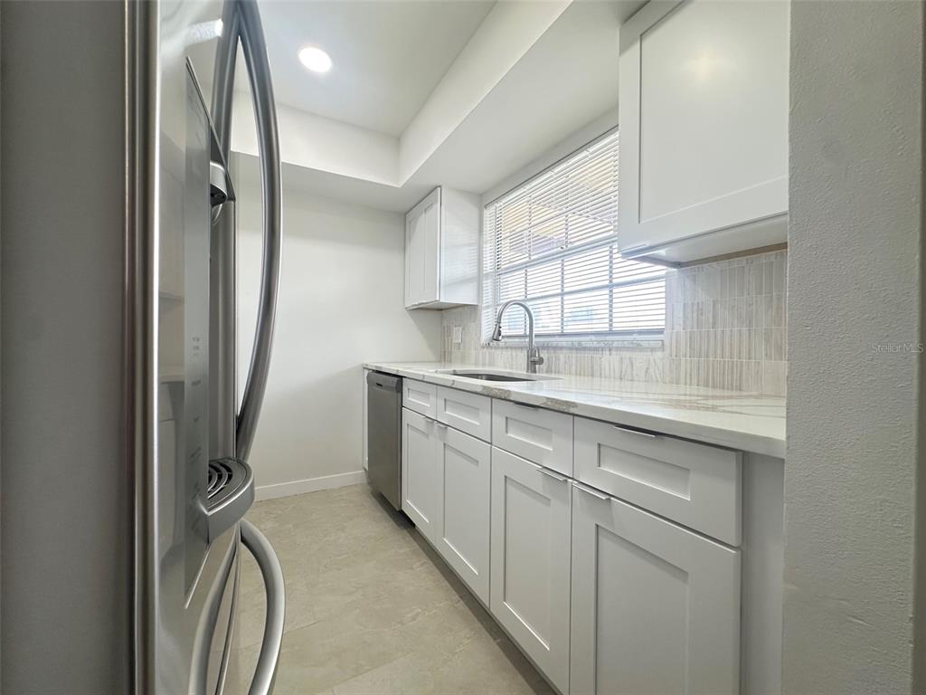A galley kitchen features white cabinets, light countertops, a stainless steel dishwasher, and a window — 1845 S HIGHLAND AVENUE UNIT 6-11, CLEARWATER, FL