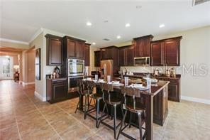A kitchen features dark wood cabinets, a large center island with bar stools, and tile flooring — 9269 OUTLOOK ROCK TRAIL, WINDERMERE, FL