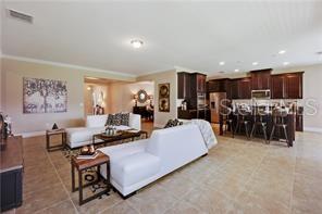 An open-concept living room features white sofas, tile flooring, and a kitchen with dark cabinetry — 9269 OUTLOOK ROCK TRAIL, WINDERMERE, FL