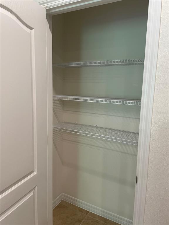 A pantry closet features white wire shelving mounted on plain walls above a tiled floor — 1249 YELLOW FINCH DRIVE, DAVENPORT, FL