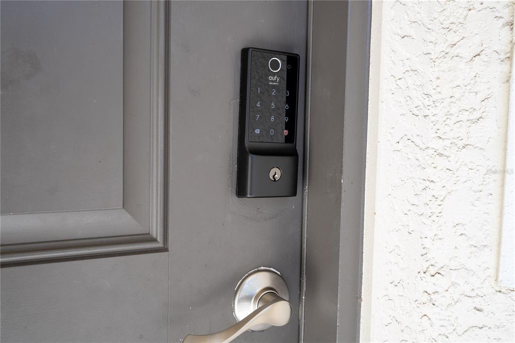 A dark gray front door features a black eufy smart lock and a silver handle — 4554 ALBERTO CIRCLE, KISSIMMEE, FL