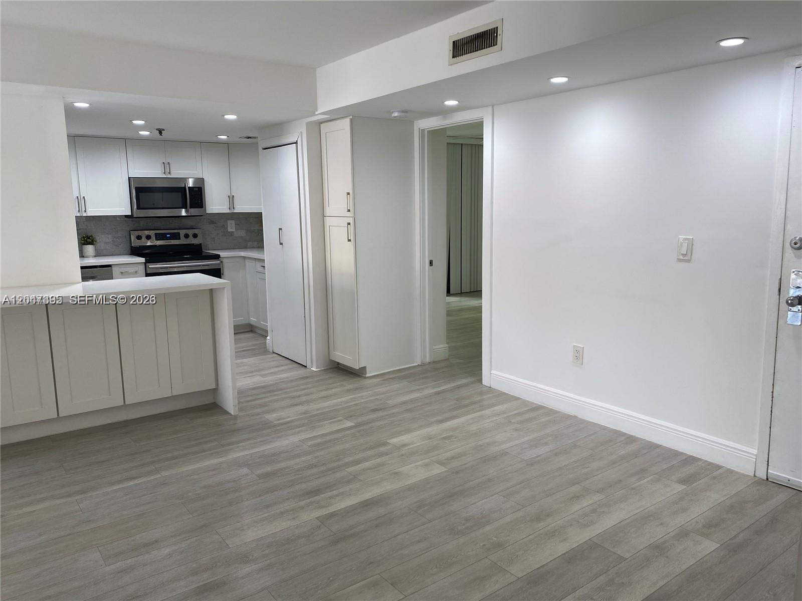 A kitchen with white cabinets and a breakfast bar opens into a living area — 911 E Ponce De Leon Blvd # 301, Coral Gables FL 33134, CORAL GABLES, FL