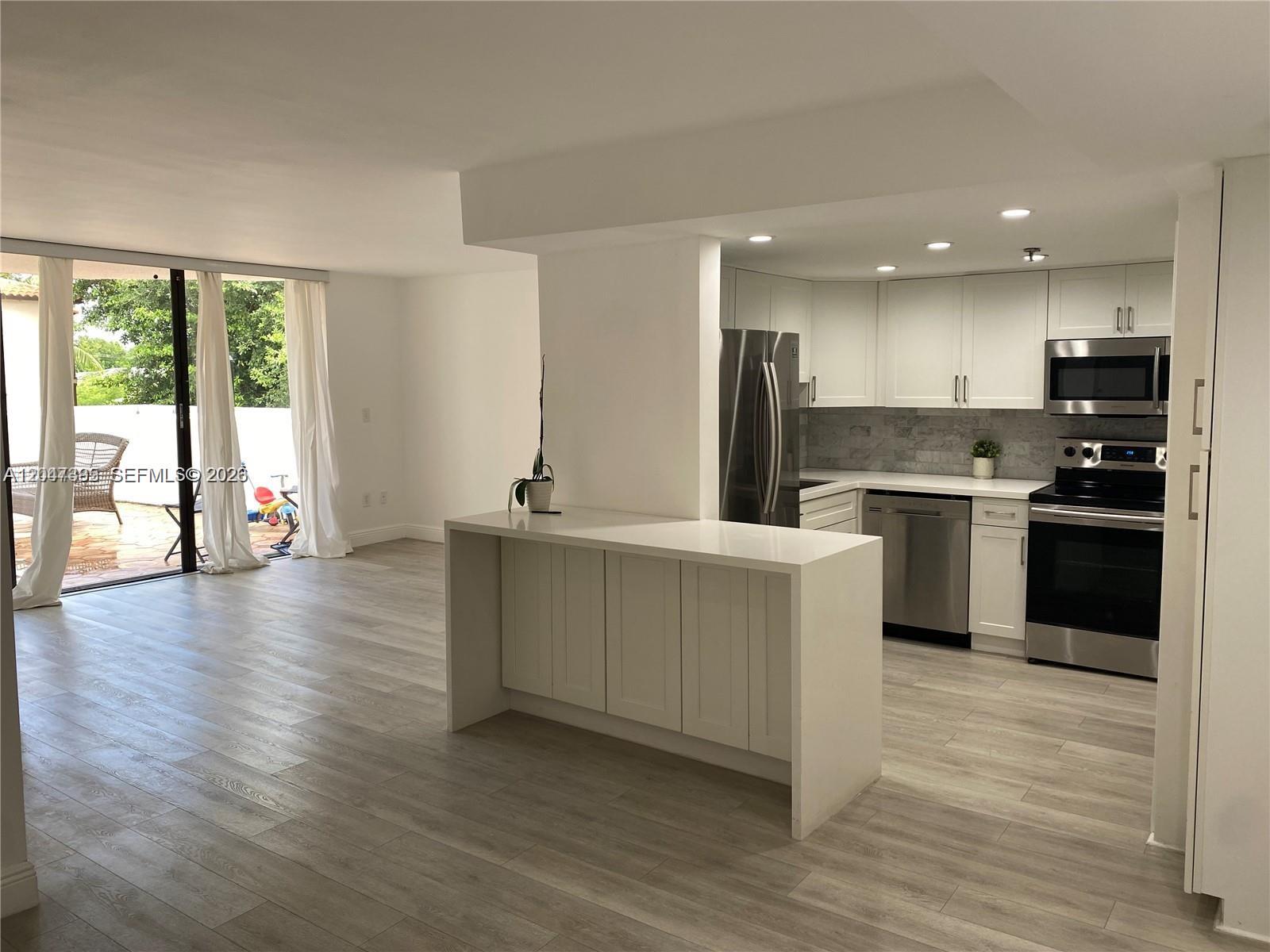 A kitchen with white cabinets and stainless steel appliances opens to a living area — 911 E Ponce De Leon Blvd # 301, Coral Gables FL 33134, CORAL GABLES, FL