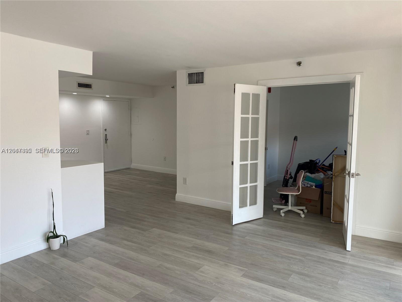 An interior view shows a room with light wood-look flooring, white walls, and French doors — 911 E Ponce De Leon Blvd # 301, Coral Gables FL 33134, CORAL GABLES, FL
