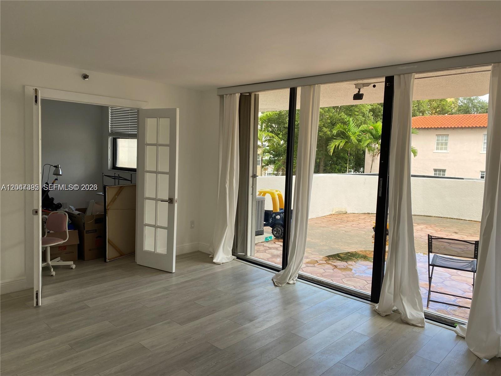 A room with light wood-look flooring features a glass sliding door opening to a patio — 911 E Ponce De Leon Blvd # 301, Coral Gables FL 33134, CORAL GABLES, FL