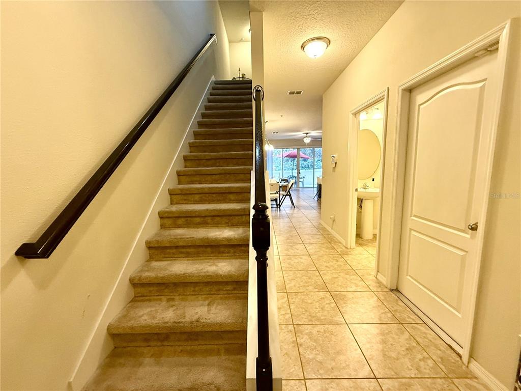 A carpeted staircase leads upstairs next to a tiled hallway with a bathroom and door — 7522 ALOMA PINES COURT, WINTER PARK, FL