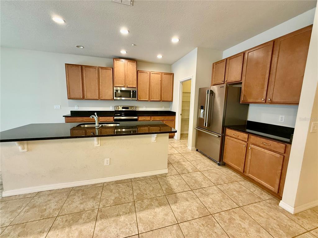 A kitchen features light-colored walls, wood cabinets, black countertops, and stainless steel appliances — 7522 ALOMA PINES COURT, WINTER PARK, FL