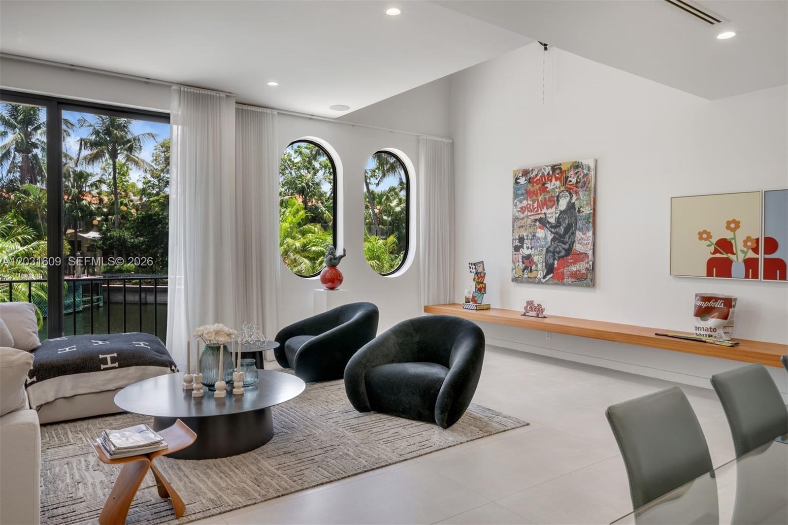 A modern living room features two dark armchairs, arched windows, and a long wooden shelf — 10659 NE Quaybridge Ct # C5, Miami FL 33138, MIAMI, FL