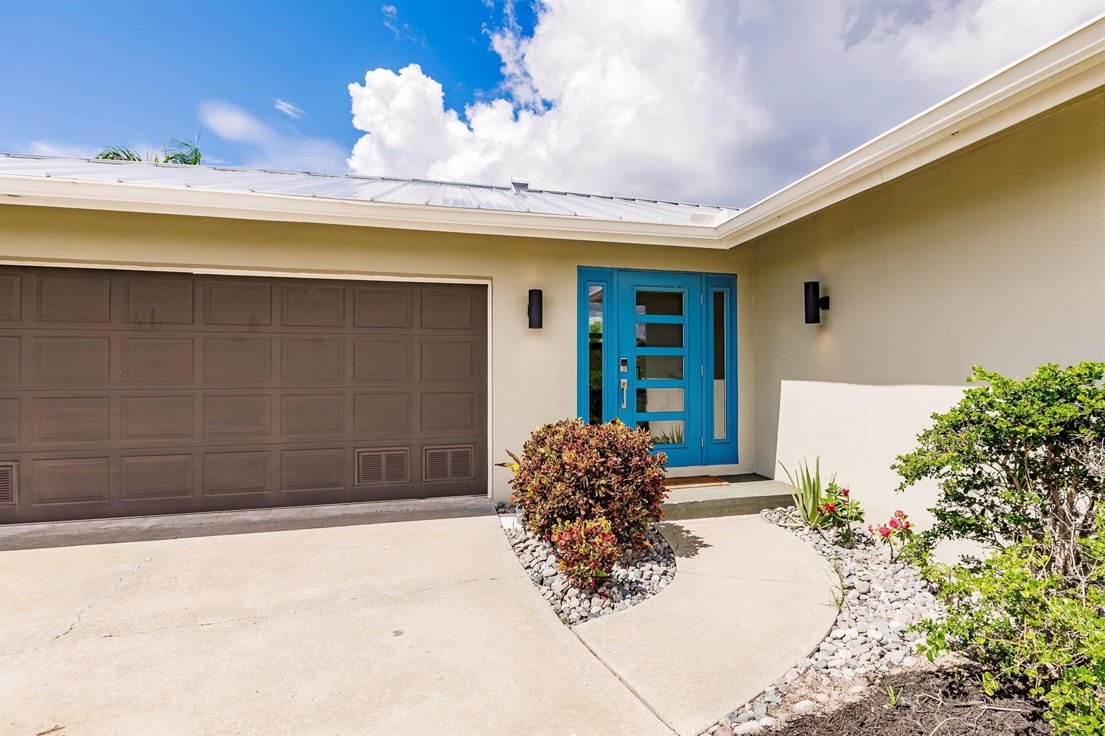 A house exterior features a brown garage door, a bright blue front door, and landscaping — 131 Casa Lane, Punta Gorda FL 33950, PUNTA GORDA, FL