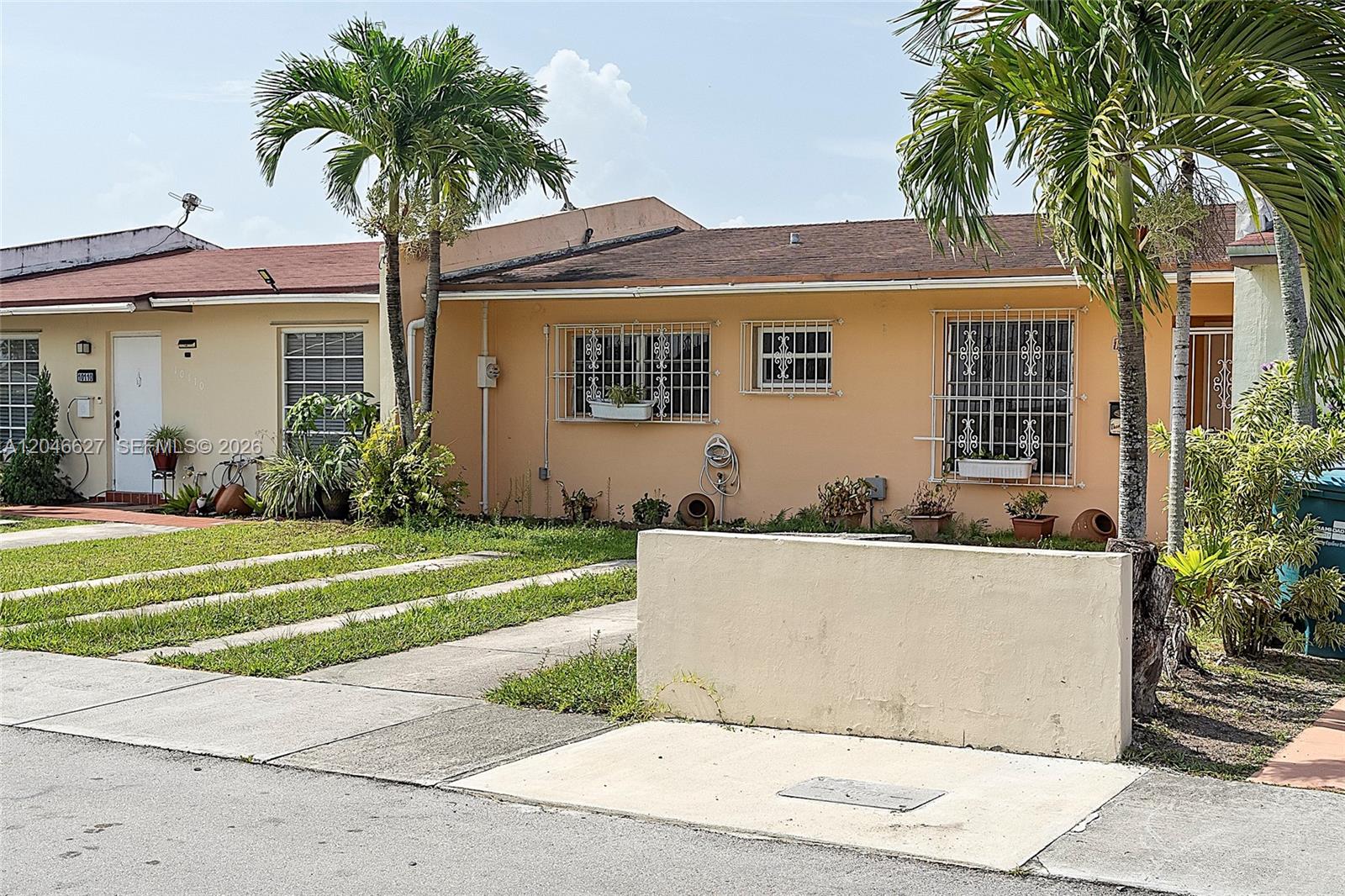 A peach-colored single-story house features a concrete driveway, palm trees, and security bars on windows — 10112 SW 23rd St, Miami FL 33165, MIAMI, FL