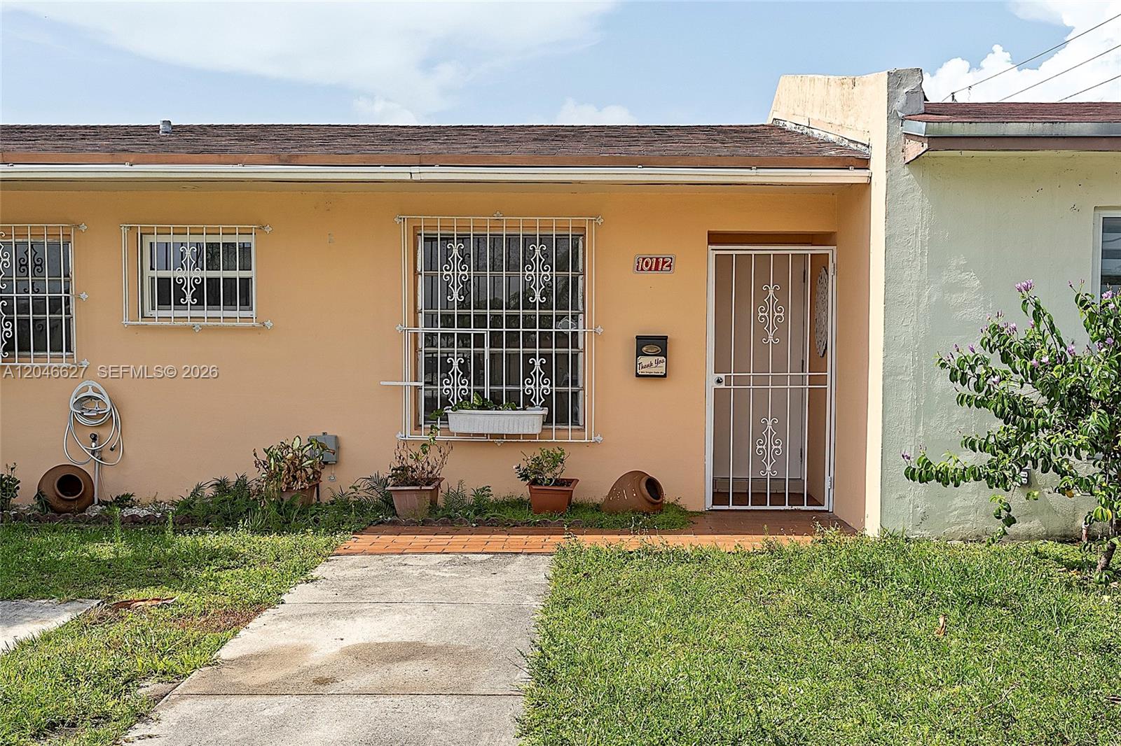 The exterior of a peach-colored house features security bars on the windows and front door — 10112 SW 23rd St, Miami FL 33165, MIAMI, FL