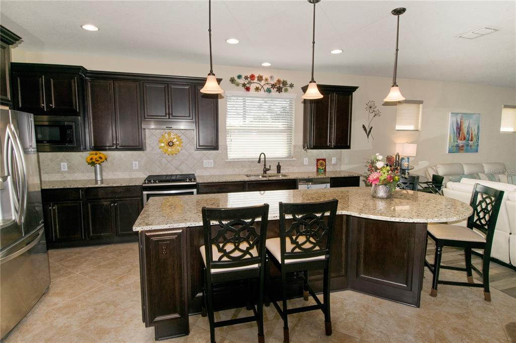A kitchen features dark wood cabinets, granite countertops, a large island, and three pendant lights — 715 ASTURIAS ROAD, DAVENPORT, FL