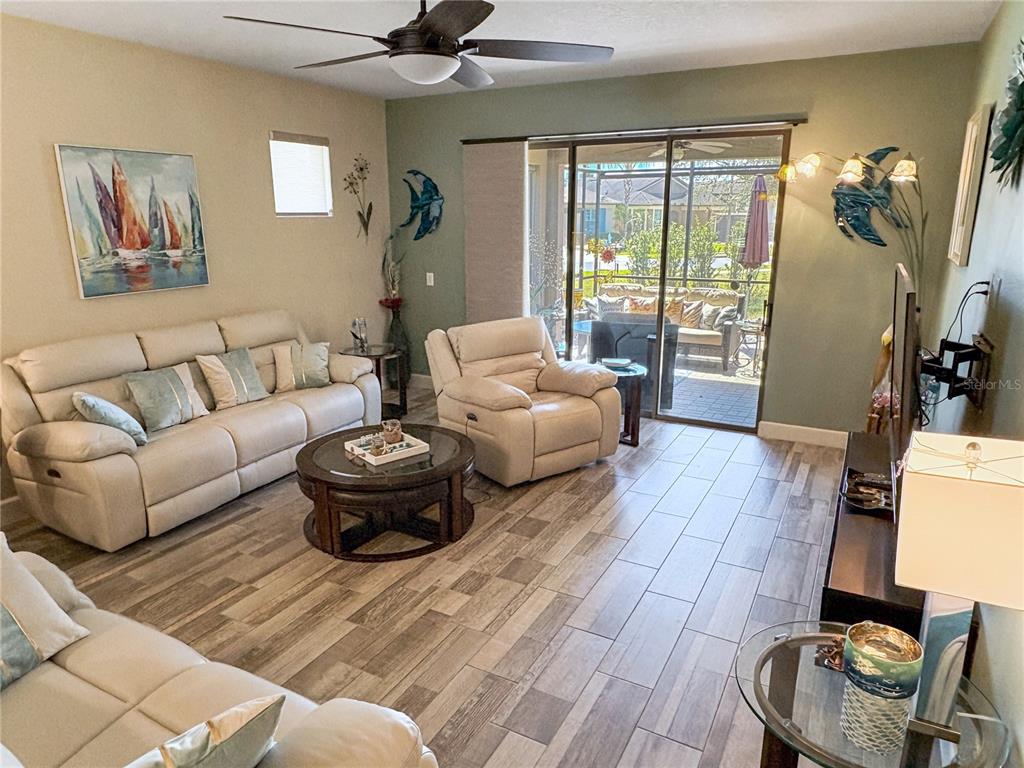 A living room features light-colored leather furniture, wood-look tile flooring, and sliding glass doors — 715 ASTURIAS ROAD, DAVENPORT, FL