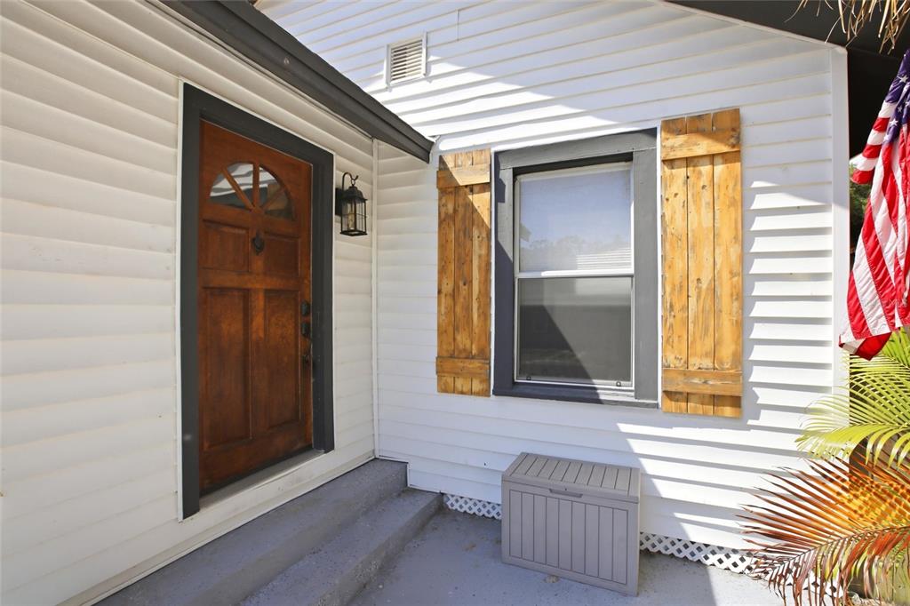 A white-sided house exterior features a wooden front door, rustic shutters, and an American flag — 4551 19TH AVENUE S, ST PETERSBURG, FL