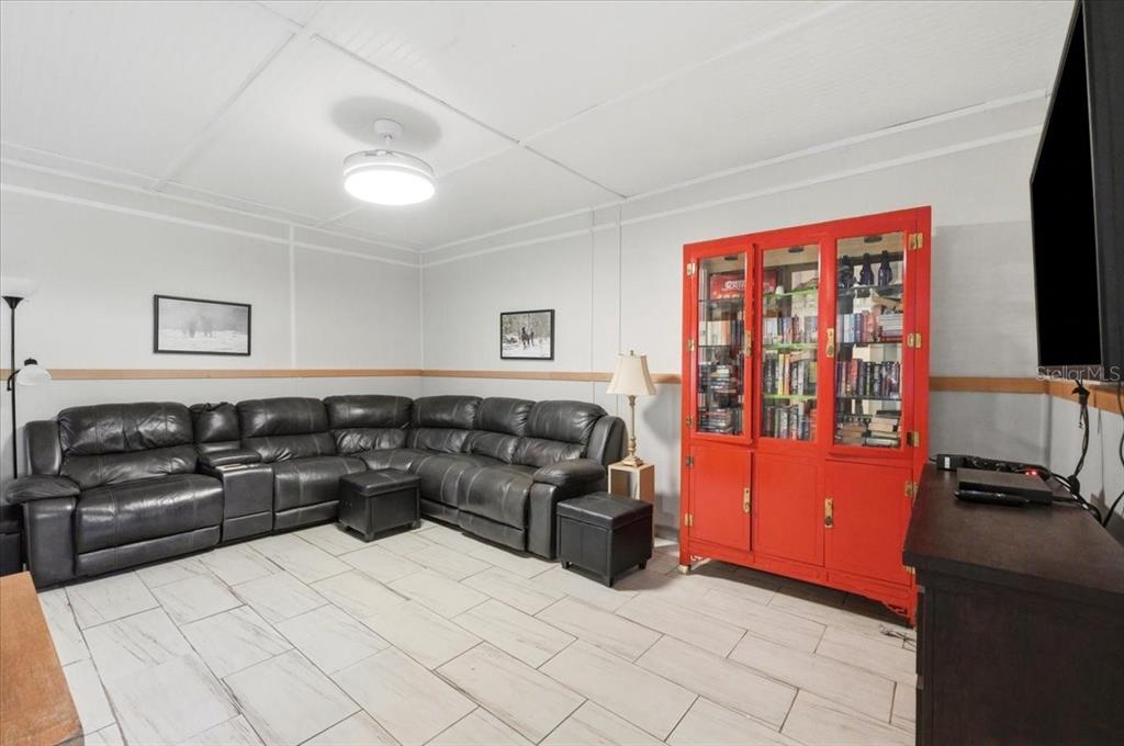 A living room features a large black sectional sofa, a bright red cabinet, and tiled flooring — 1425 PIONEER DRIVE, LAKELAND, FL