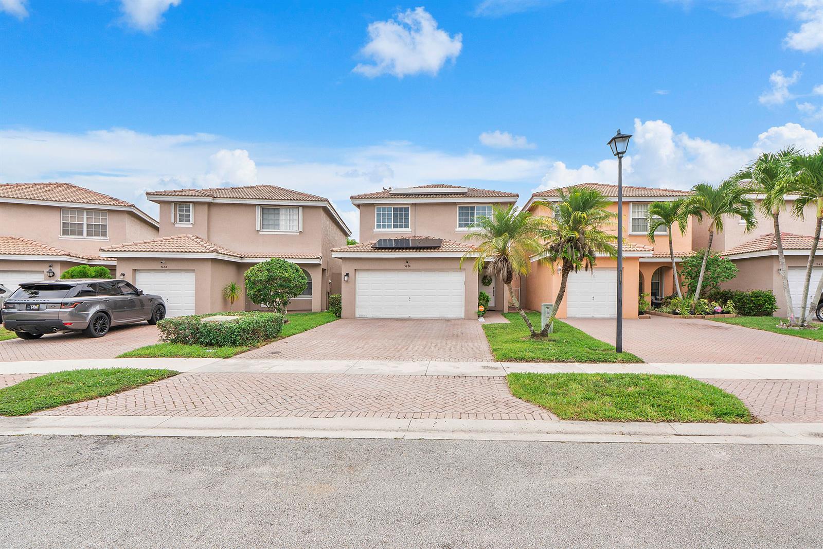 A row of suburban two-story houses with paved driveways and palm trees under a blue sky — 5474 NW 94th Terrace, Sunrise FL 33351, SUNRISE, FL