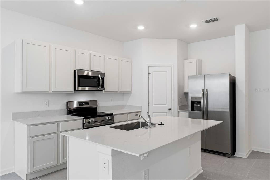 A modern kitchen features white cabinetry, stainless steel appliances, and a large central island — 3143 KURTZ TERRACE, DAVENPORT, FL