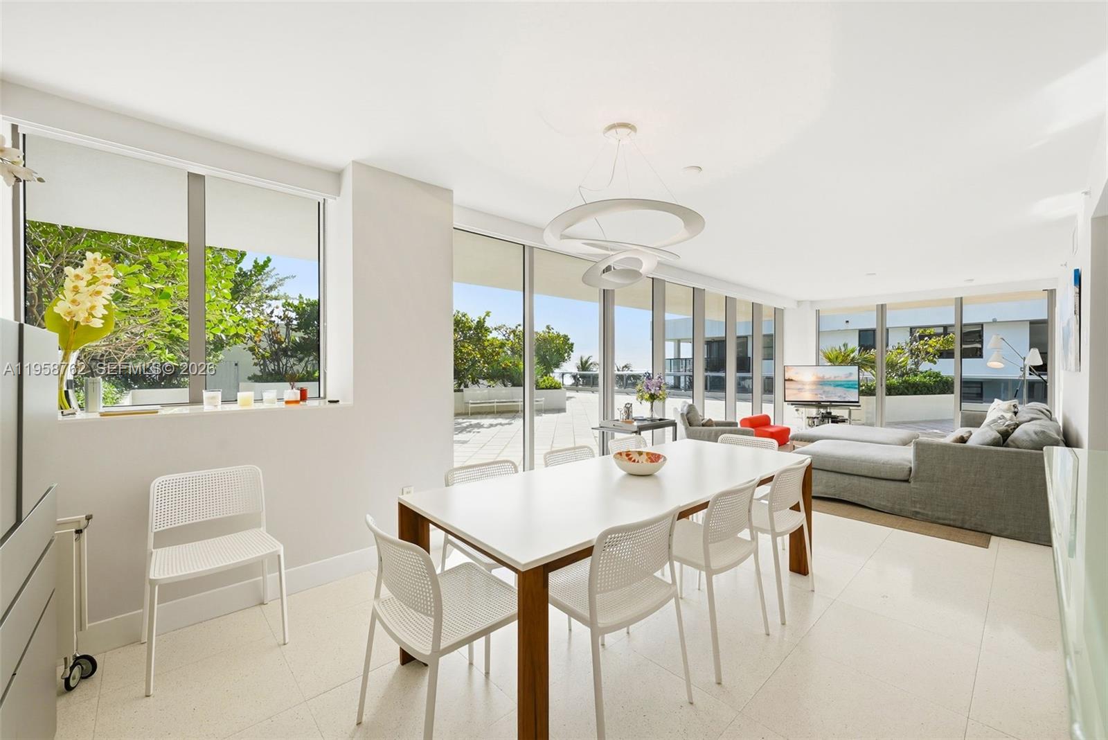 A bright dining and living area features white tile floors, floor-to-ceiling windows, and modern furniture — 5875 Collins Ave # 502, Miami Beach FL 33140, MIAMI BEACH, FL